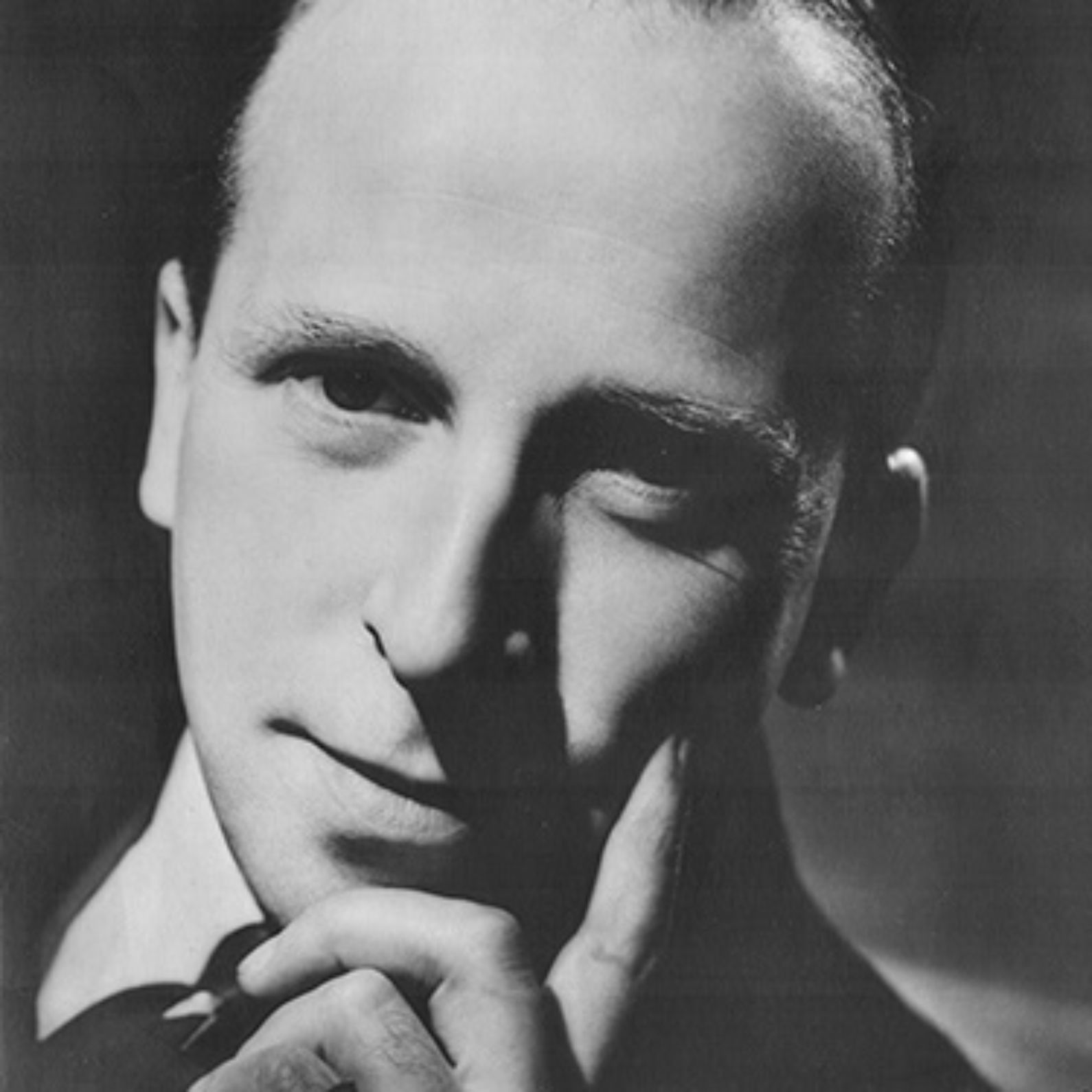 A portrait of theatre founder John Stewart in black and white with one hand placed upon his face and looking directly into camera