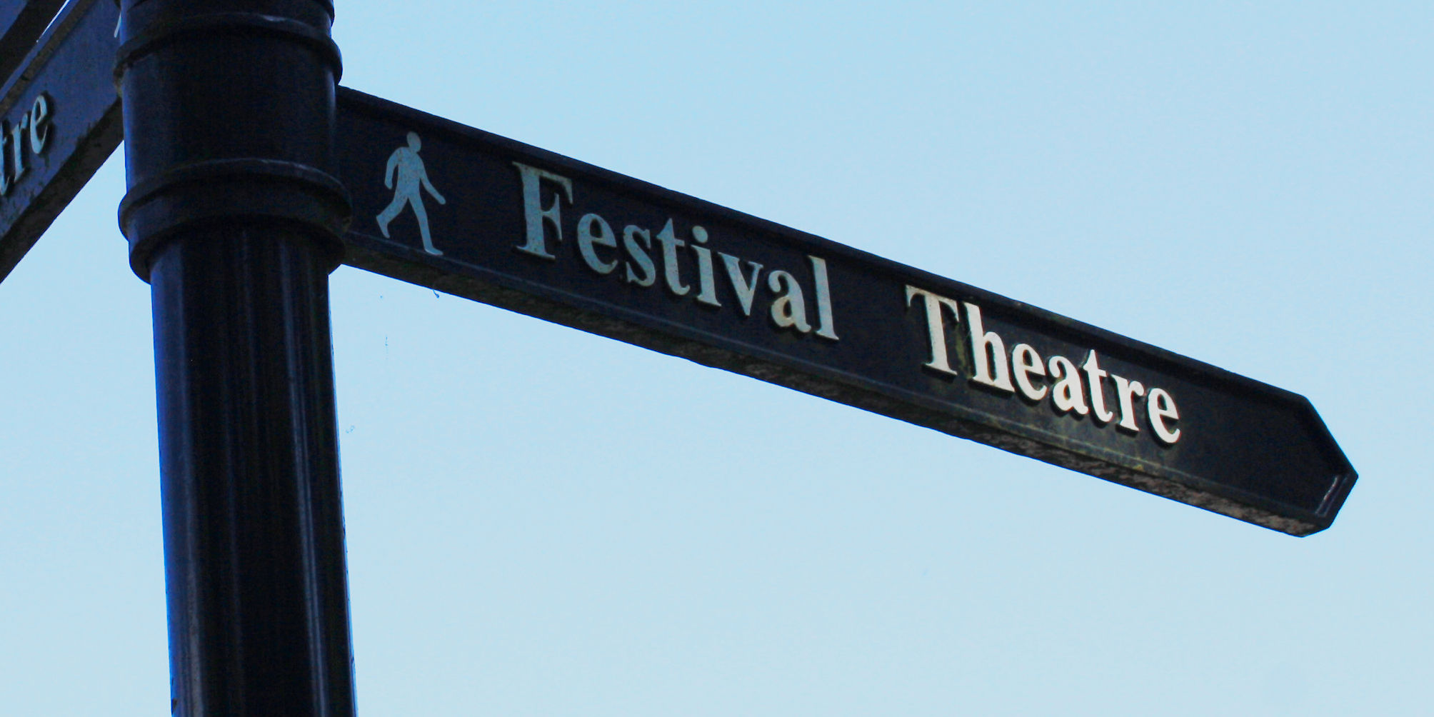 A Black sign post that points in the direction towards Pitlochry Festival Theatre in White writing, there is also an image of a person walking on the left hand side of the words.