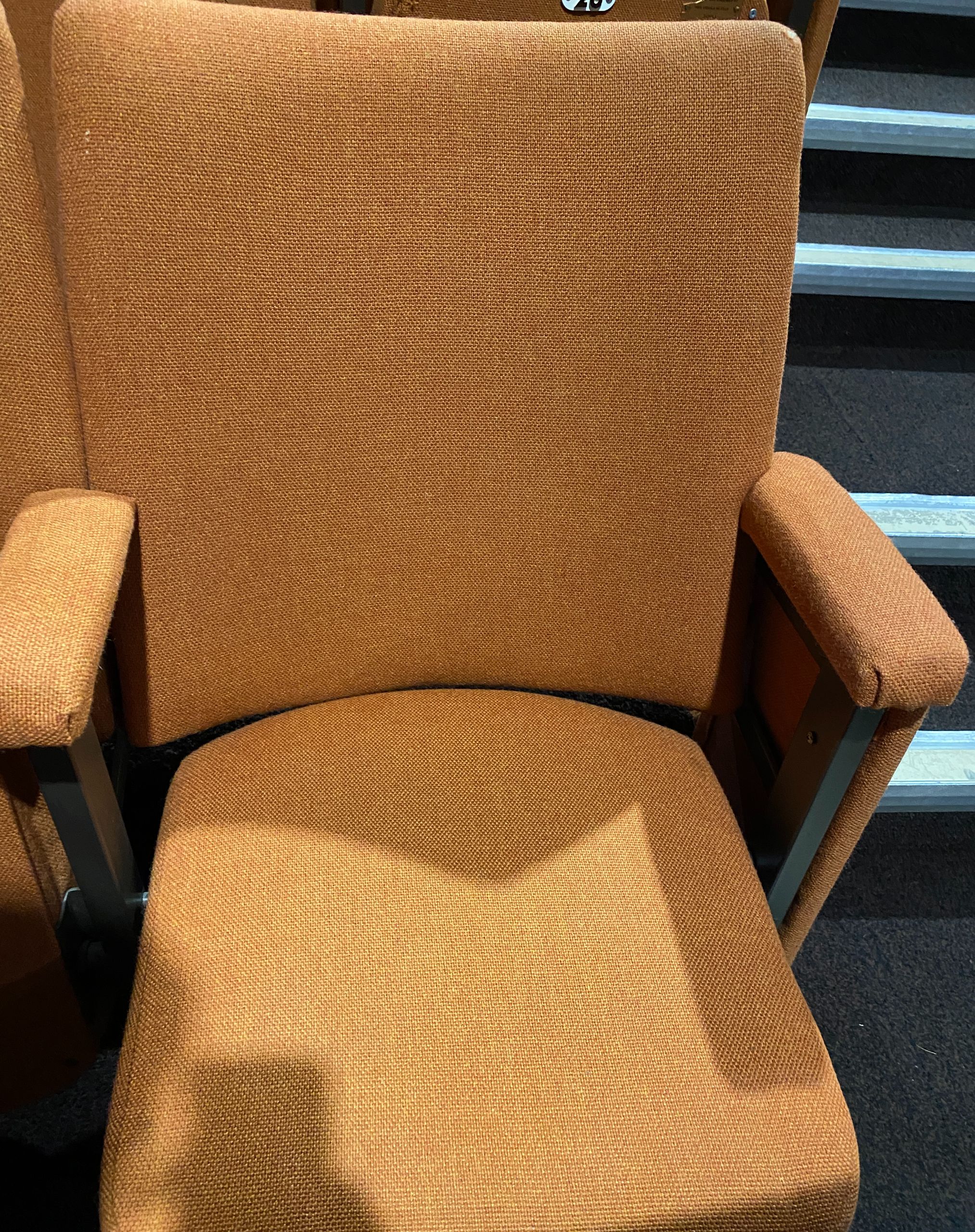 An image of a light orange folding theatre chair with arm rests.